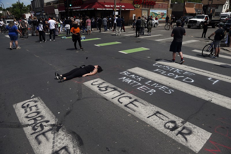 A woman lies in the street as protesters gather Wednesday, May 27, 2020 near the site of the arrest of George Floyd who died in police custody Monday in Minneapolis after video shared online by a bystander showed a white officer kneeling on his neck during his arrest as he pleaded that he couldn't breathe. (AP Photo/Jim Mone)