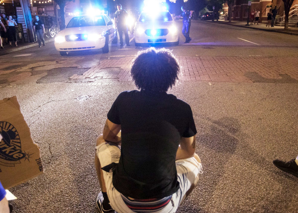 Staff photo by Troy Stolt / A protester kneels as Chattanooga Police officers get out of their cars, Saturday night, on Frazier Avenue during protests over the murder of George Floyd by Minneapolis police officers.