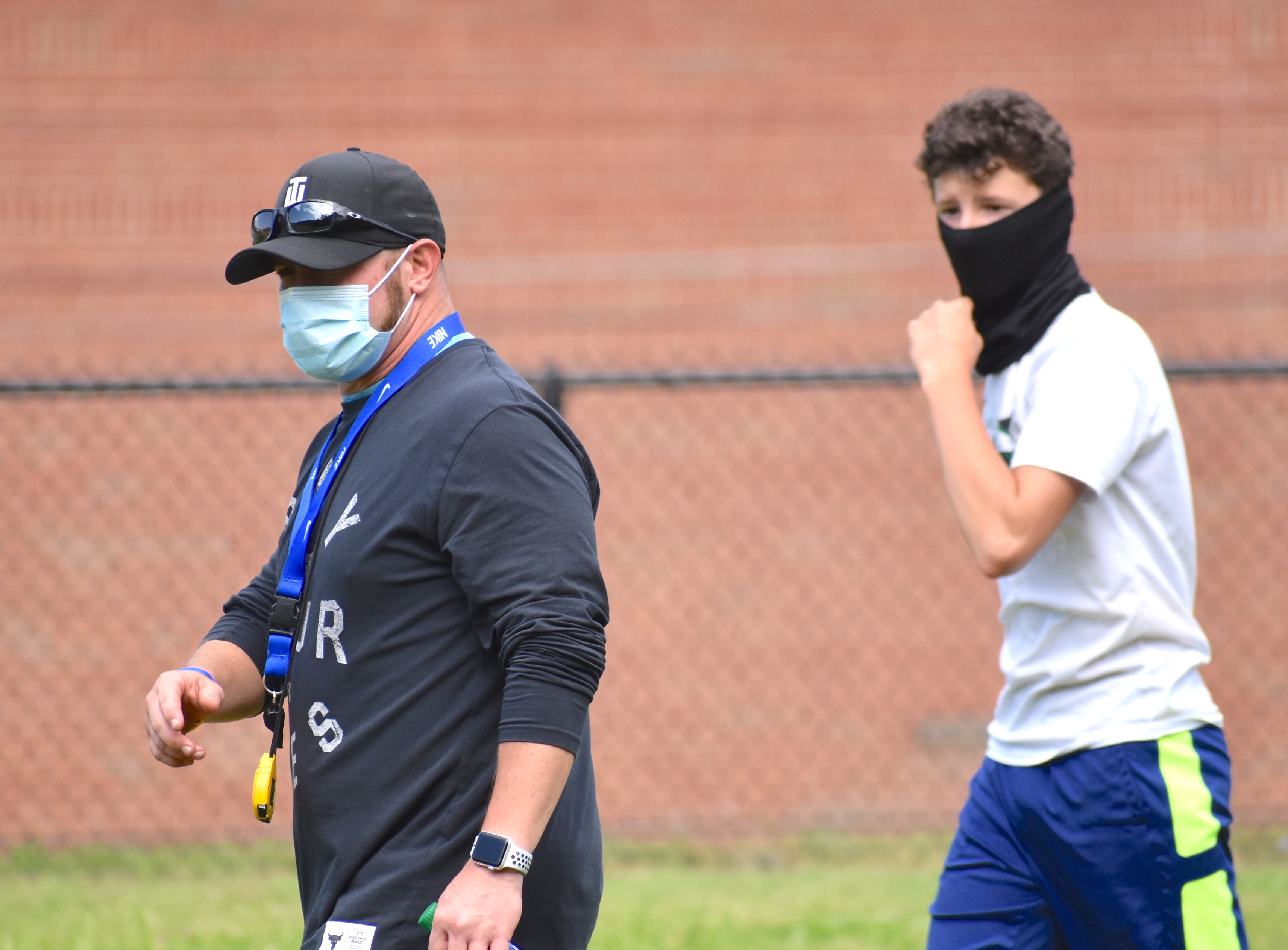 Staff photo by Patrick MacCoon / Red Bank High School football assistant coach Brad Cowell and sophomore Jake Brune walk off the field wearing protective masks during practice Monday.