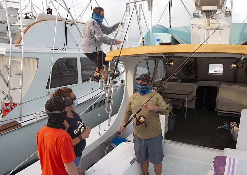 In this photo provided by the Florida Keys News Bureau, Captain Glenn Miller climbs to the bridge on his sport fishing boat GonFishin V; while mate Josh Rabon, right, explains to his guests what to expect during the planned day of fishing off the Florida Keys Monday, June 1, 2020, in Islamorada, Fla. After being closed to visitors since March 22 to help curtail the spread of COVID-19, the Keys reopened Monday. Tourism employs about 45 percent of the Keys workforce. (Andy Newman/Florida Keys News Bureau via AP)