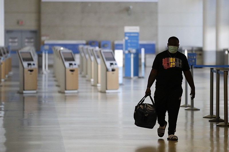 A traveler walks in a mostly empty American Airlines terminal at the Los Angeles International Airport, Thursday, May 28, 2020, in Los Angeles. From Britain's EasyJet to American and Delta in the U.S., airlines are cutting even more jobs to cope with a crushing drop in air travel caused by the coronavirus pandemic. (AP Photo/Marcio Jose Sanchez)