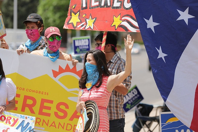 Democratic congressional candidate Teresa Leger Fernandez, in the blue mask, cheers on supporters at a polling station Tuesday, June 2, 2020, in Santa Fe, N.M. Fernandez was flanked by her three sons, left to right, Alisandro, Dario and Abelino. The sign she holds, "Ahora es cuando," is Spanish for "Now is the time." (AP Photo/Cedar Attanasio)