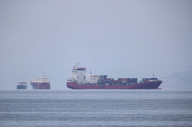 A cargo ship approaches the port of Piraeus as other ships are anchored, near Athens, Greece, Tuesday, May 26, 2020. During the new coronavirus pandemic, about 150,000 seafarers are stranded at sea in need of crew changes, according to the International Chamber of Shipping. Roughly another 150,000 are stuck on shore, waiting to get back to work. (AP Photo/Petros Giannakouris)