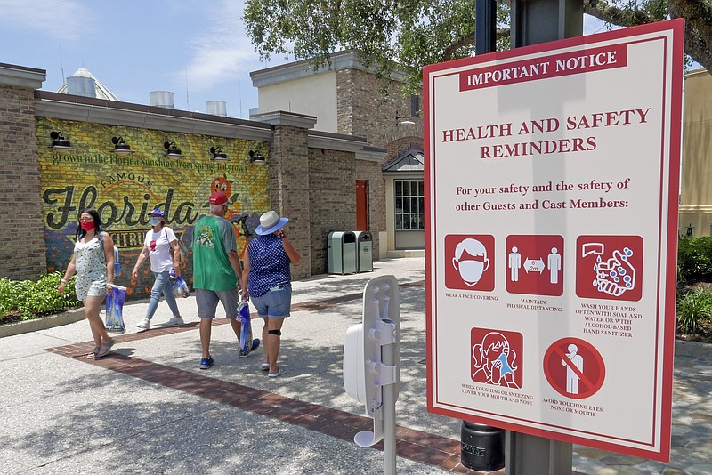 FILE - In this June 16, 2020, file photo, signs remind patrons to wear masks and other protocols because of the coronavirus pandemic as they stroll through the Disney Springs shopping, dining and entertainment complex in Lake Buena Vista, Fla. The number of deaths per day from the coronavirus in the U.S. has fallen in recent weeks to the lowest level since late March, even as states increasingly reopen for business. But scientists are deeply afraid the trend may be about to reverse itself. (AP Photo/John Raoux, File)