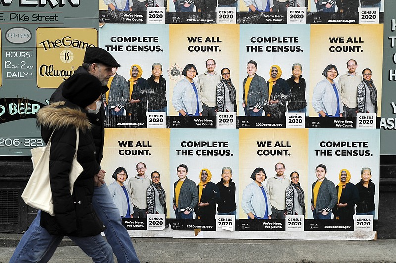 FILE - In this April 1, 2020, file photo, people walk past posters encouraging participation in the 2020 Census in Seattle's Capitol Hill neighborhood. Just how badly has the new coronavirus impacted life in the U.S.? The U.S. Census Bureau, along with five other federal agencies, will try to answer that question with a new experimental, weekly survey that just got approved earlier this week. (AP Photo/Ted S. Warren, File)