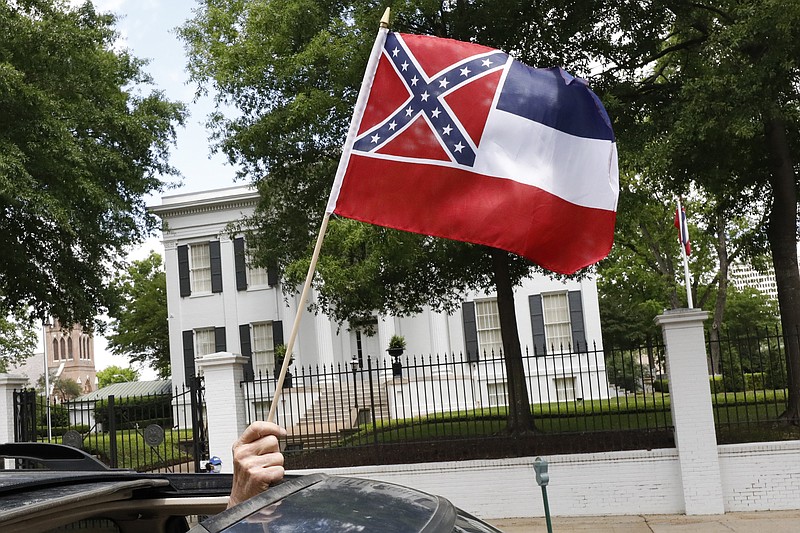 AP photo by Rogelio V. Solis / A small Mississippi state flag is held by a participant during a drive-by "reopen Mississippi" protest past the Governor's Mansion on April 25 in Jackson, Miss.