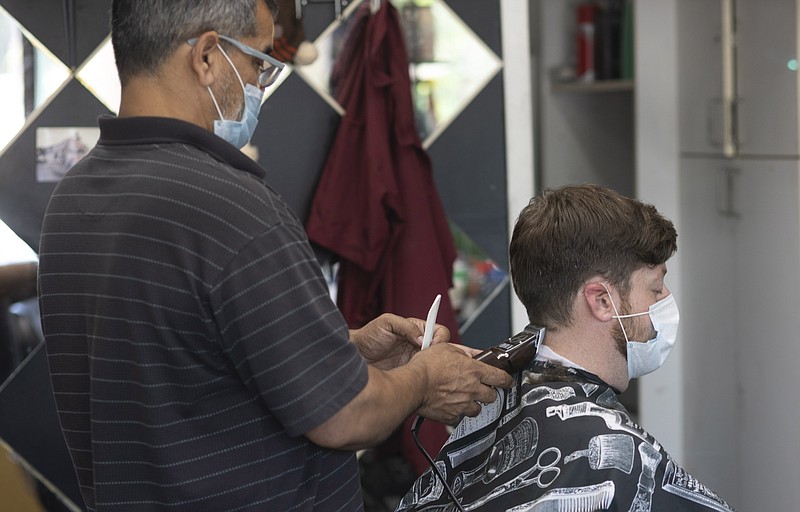 Raja Akram cuts the hair of Benjamin Brand on Monday, June 22, 2020, in the Brooklyn borough of New York. Barbershops were allowed to re-open Monday in New York City during the coronavirus pandemic. (AP Photo/David Boe)