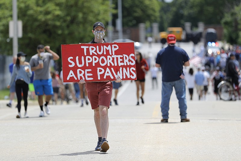 Photo by Julio Cortez of The Associated Press / A man carries a sign while walking among a crowd of people gathered outside of Fort McHenry National Monument and Historic Shrine, where President Donald Trump attended a Memorial Day ceremony on Monday, May 25, 2020, in Baltimore, Maryland.