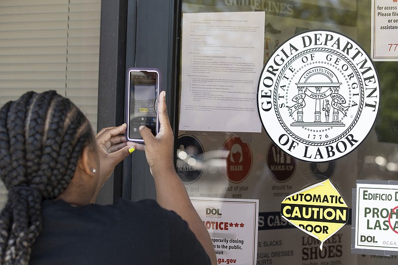 Arnashia McCain uses her phone to copy phone numbers posted on the locked doors of a Georgia Department of Labor office Thursday, May 7, 2020, in Norcross Ga. McCain, who said she drives for Lyft and has had her hours cut in her job in retail, has been unable check on the status of her her unemployment claim. (AP Photo/John Bazemore)


