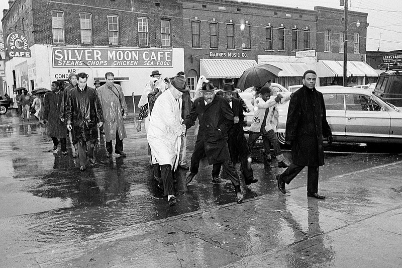 FILE - In this March 1, 1965 file photo Dr. Martin Luther King Jr. hops over a puddle as it rains in Selma, Ala. King led hundreds of African Americans to the court house in a voter registration drive. At front is civil rights worker Andrew Young, and at right, behind King is Rev. Ralph Abernathy. Today's protests across America against racial injustice are being watched closely by people who five decades ago faced jail cells, bloody assaults, snarling dogs and even potential assassination in the battle against institutional racism. Young, a King lieutenant, marvels at both the sizes and the spontaneity of the protests. The former Democratic congressman, Atlanta mayor and United Nations ambassador recalled activists spending three months to organize for a 1963 Birmingham, Alabama, campaign in which King and other protesters were jailed. (AP Photo, File)