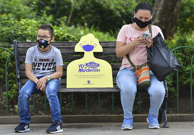 The Associated Press / A woman and child wear masks and maintain a distance between each other while on a park bench in Medellin, Colombia.
