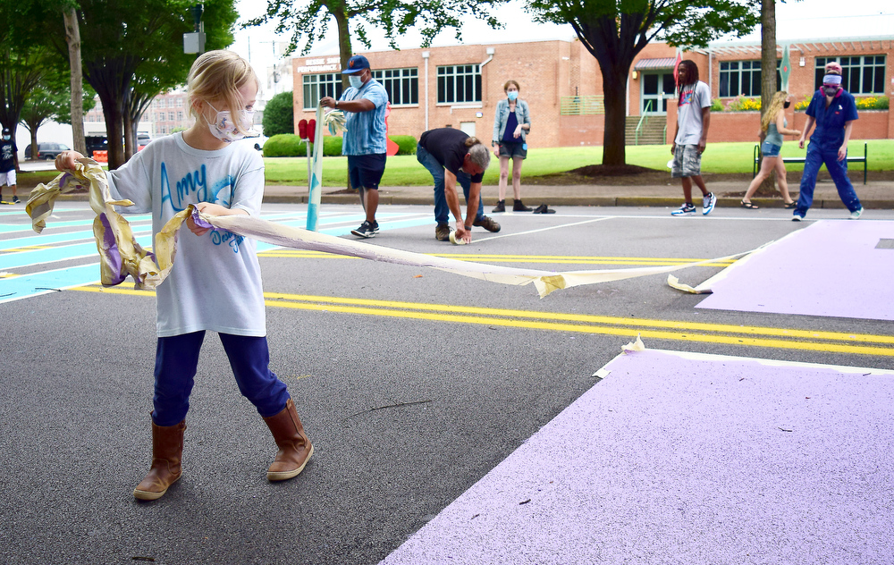 Staff Photo by Robin Rudd / Briony Brauer removes tape from a finished portion of the mural on Martin Luther King Jr. Blvd.. In the background stands the Bessie Smith Cultural Center.