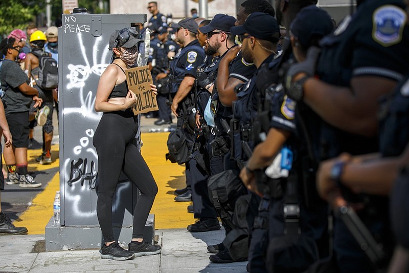 FILE - In this June 23, 2020 file photo, A woman holds up a sign saying "police the police" as she confronts a police line while demonstrators protest in Washington, over the death of George Floyd. Without major changes in almost every state, a national police misconduct database like what the White House and Congress have proposed after George Floyd's death would fail to account for thousands of problem officers. (AP Photo/Jacquelyn Martin File)