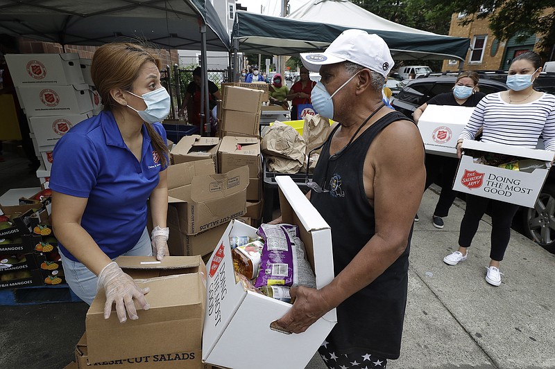 Salvation Army worker Brenda Gonzalez, of Saugus, Mass., left, distributes food to an unidentified man while others impacted by the coronavirus wait in line at a Salvation Army center, Tuesday, June 30, 2020, in Chelsea, Mass. (AP Photo/Steven Senne)


