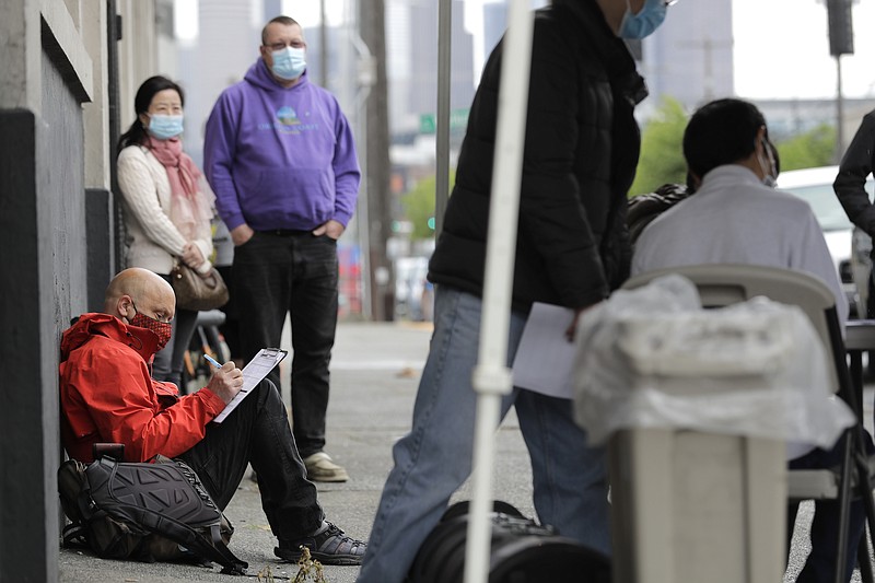 In this Saturday, May 16, 2020, file photo, Glen Buhlmann, lower left, fills out a job application during a walk- and drive-up job fair in Seattle for clothing maker Outdoor Research's new line of face masks and other personal protection equipment the company has started manufacturing due to the coronavirus pandemic. U.S. employers likely rehired several million more workers in June, thereby reducing a Depression-level unemployment rate, but the most up-to-date data suggests that a resurgent coronavirus will limit further gains. (AP Photo/Ted S. Warren, File)

