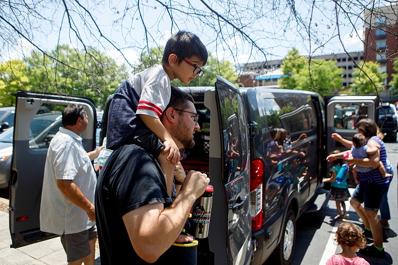 Staff photo by C.B. Schmelter / Carrying his 4-year-old son Killian on his shoulders, Dallas Tharp and his family, along with his wife's parents, load up in a van at the Tennessee Aquarium on Thursday. The family was traveling from the Midwest to North Georgia for a family reunion.