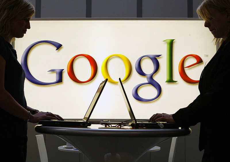 FILE- / Google employee work on laptop computers in front of an illuminated sign of the Google logo