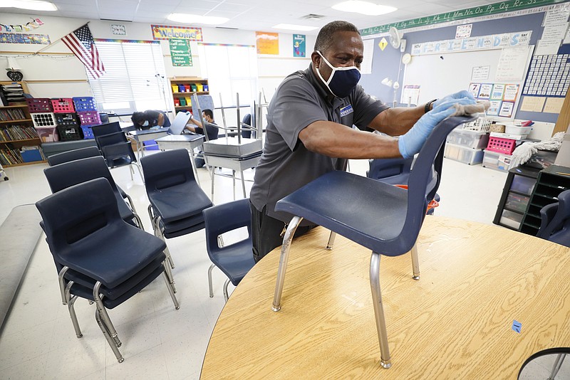 Des Moines Public Schools custodian Tracy Harris cleans chairs in a classroom at Brubaker Elementary School, Wednesday, July 8, 2020, in Des Moines, Iowa. Getting children back to school safely could mean keeping high-risk spots like bars and gyms closed. That's the latest thinking from some public health experts. (AP Photo/Charlie Neibergall)