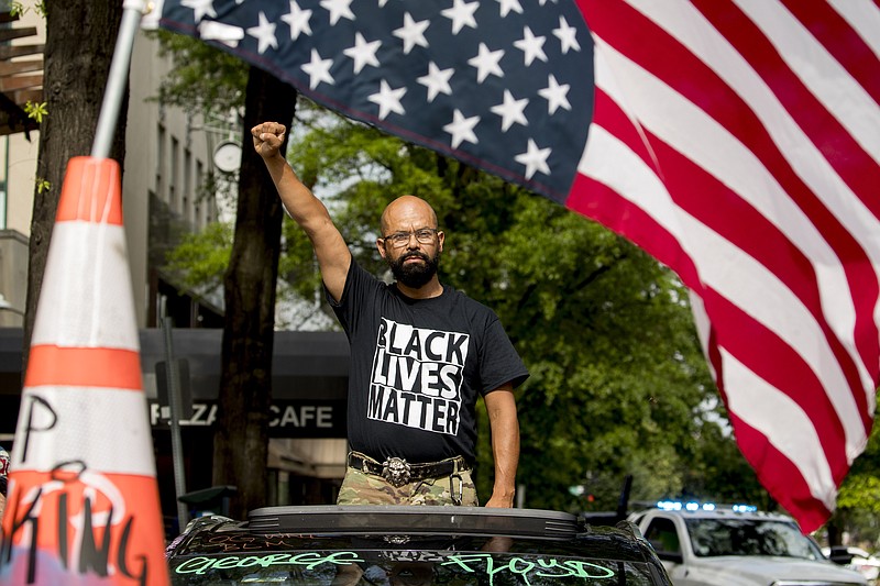 George Floyd's name is written on the windshield as John Coy wears a shirt that reads Black Lives Matter and stands through his sunroof with his fist in the air at 16th Street Northwest renamed Black Lives Matter Plaza near the White House, Friday, June 19, 2020, in Washington. (AP Photo/Andrew Harnik)