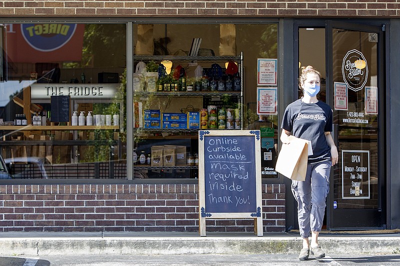 Staff photo by C.B. Schmelter / Retail Manager Nicole Jennings walks past a sign requiring masks to be worn inside the store while bringing a curbside order to a customer at Bread & Butter Bakery on Wednesday, July 8, 2020 in Chattanooga, Tenn.