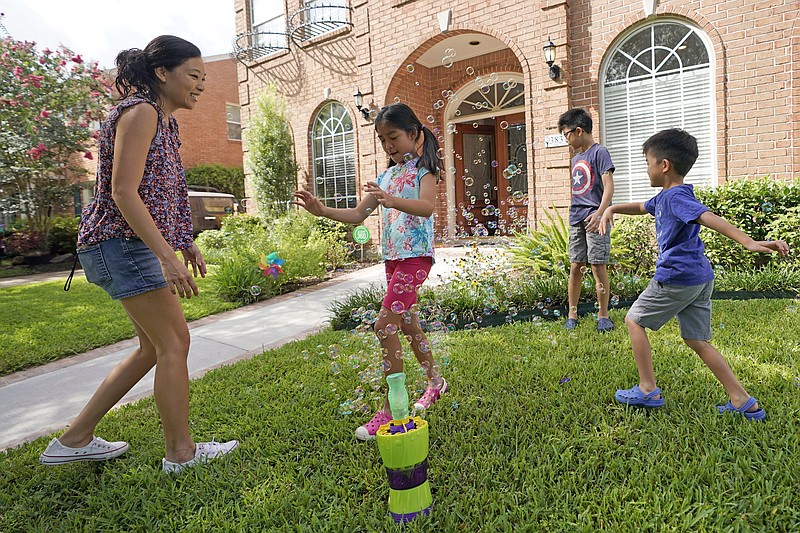 Vicky Li Yip, left, sets up a bubble machine for her children, left, to right, Kelsey, 8, Toby, 10 and Jesse, 5, outside their home, Friday, July 10, 2020, in Houston. Vicky Li Yip works from home and says online schooling has been exhausting, even with her husband helping out. But with her city becoming a national hot spot, she has been considering what it would mean for her children to face possible exposure every day. (AP Photo/David J. Phillip)