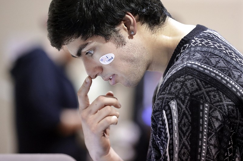 David Flores-Figueroa wears his voting sticker on his face as he reads over the ballot before voting on Super Tuesday at the Cleveland Park Community Center precinct, Tuesday, March 3, 2020, in Nashville, Tenn. Deadly overnight tornadoes delayed the start of the presidential primary voting in Nashville and another Tennessee county, spurring elections officials to redirect voters from some polling places to alternate locations. Voters from six precincts were combined to vote at Cleveland Park, where the wait could take up to an hour or more. (AP Photo/Mark Humphrey)