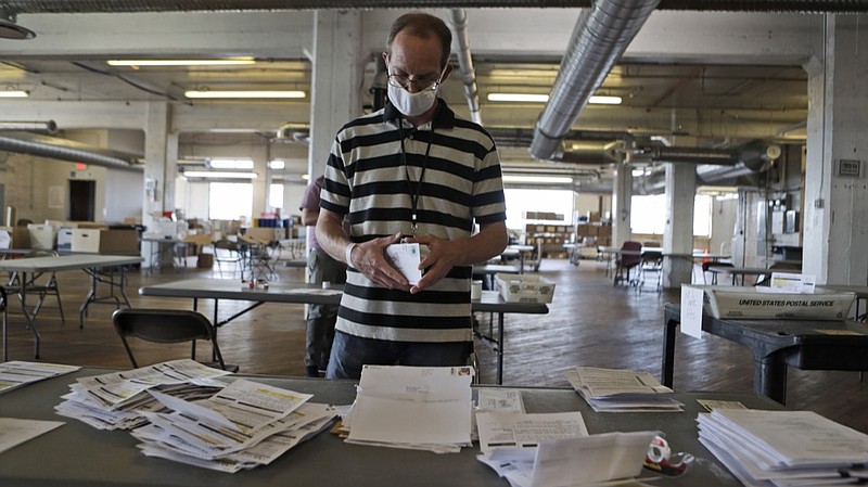 Mike Babinski opens applications for voter ballots at the Cuyahoga County Board of Elections Tuesday, July 14, 2020, in Cleveland. As more states embrace mail-in balloting, an often overlooked detail has emerged as a partisan dividing line: postage. Questions over whether postage will be required for absentee ballot applications and ballots themselves, who pays for it and what happen to envelopes without stamps are the subject of lawsuits and Statehouse political brawls. (AP Photo/Tony Dejak)