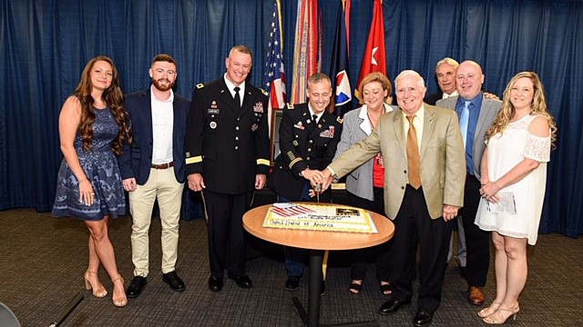 Contributed photo by Army Materiel Command / Lt. Col. Burt Fisher cuts a cake during his military retirement ceremony with a Japanese sword his grandfather, J.W. Burton, brought back from World War II in 1945. From left are Chelsea Zimmerman; Gage Fisher; Maj. Gen. Robert Harter; Burt, Miriam and Randy Fisher; J. Breton Burton; and Matt and Stacey Fisher.