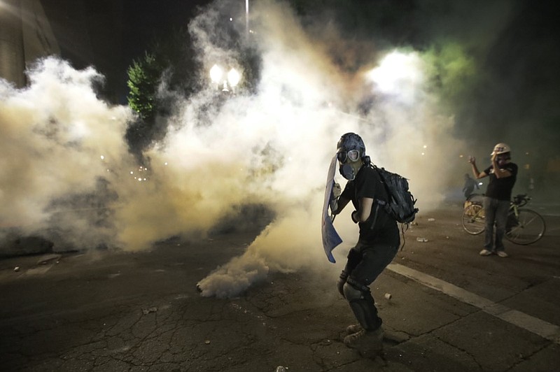 A demonstrator tries to shield himself from tear gas deployed by federal agents during a Black Lives Matter protest at the Mark O. Hatfield United States Courthouse Wednesday, July 29, 2020, in Portland, Ore. (AP Photo/Marcio Jose Sanchez)

