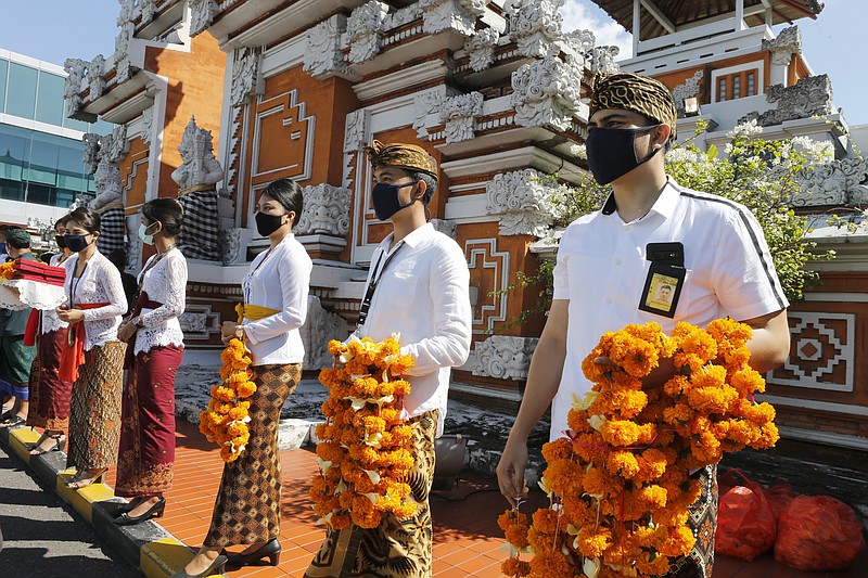 Airport officers wearing face masks line up as they hold flowers to welcome passengers at Bali airport, Indonesia on Friday, July 31, 2020. Indonesia's resort island of Bali reopened for domestic tourists after months of lockdown due to a new coronavirus. (AP Photo/Firdia Lisnawati)