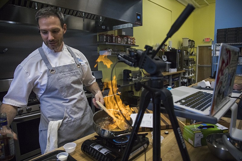 Staff photo by Troy Stolt / Instructor Jeff Pennypacker ignites his pan with cooking sherry as he teaches a cooking class through the video call app Zoom at the Sweet & Savory Classroom, 45 E. Main St.