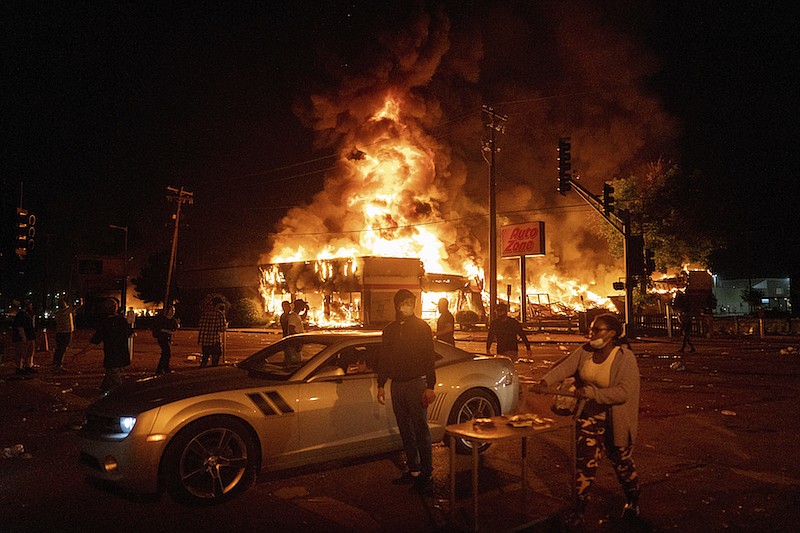 An AutoZone store burns as protesters gather outside of the Third Precinct in Minneapolis Thursday, May 28, 2020. Police say a man captured on surveillance video breaking windows at a south Minneapolis auto parts store in the days after George Floyd's death is a Hell's Angels member who was bent on stirring up social unrest. Minneapolis police spokesman John Elder told The Associated Press on Tuesday, July 28, 2020 that the investigation remains open and active and that he could not confirm the name of the person involved. (Mark Vancleave/Star Tribune via AP)