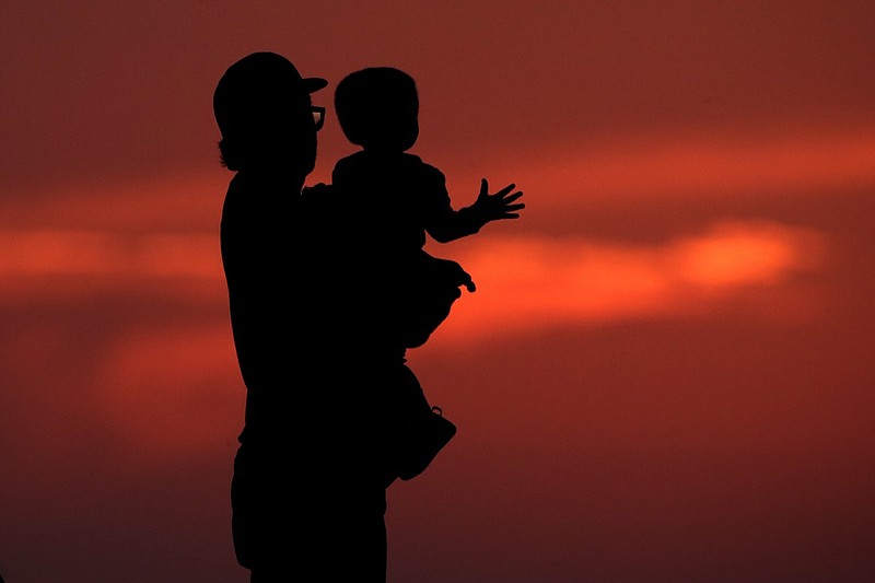 FILE - In this June 26, 2020 file photo, a man and his son are silhouetted against the sky as they watch the sunset from a park in Kansas City, Mo. Health experts once thought 2020 might be the worst year yet for a rare paralyzing disease that has been hitting U.S. children for the past decade. But they now say the coronavirus pandemic could disrupt the pattern for the mysterious illnesses, which spike every other year starting in late summer. (AP Photo/Charlie Riedel, File)