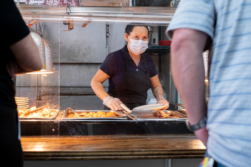 Tucker-Marie Rodriguez helps a customer from behind acrylic panels during the lunch rush at Matthews Cafeteria on Main Street in Tucker on Friday afternoon July 17, 2020. The dining institution, established in 1955, ask customers to wear masks, added the acrylic dividers, made separate entrance and exit doors and have drive-up service. / Ben Gray for the Atlanta Journal-Constitution