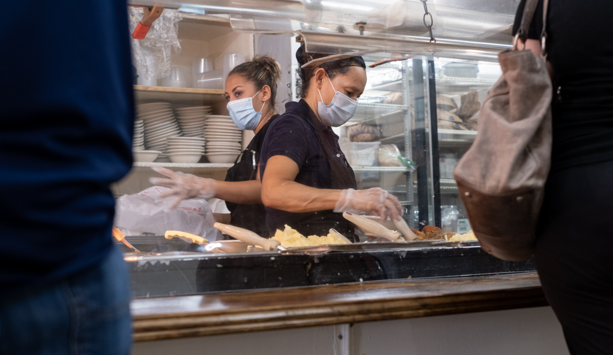Tucker-Ingred Cruez, left, and Marie Rodriguez help customers from behind acrylic panels during the lunch rush at Matthews Cafeteria on Main Street in Tucker on Friday afternoon July 17, 2020. The dining institution, established in 1955, ask customers to wear masks, added the acrylic dividers, made separate entrance and exit doors and have drive-up service. / Ben Gray for the Atlanta Journal-Constitution.