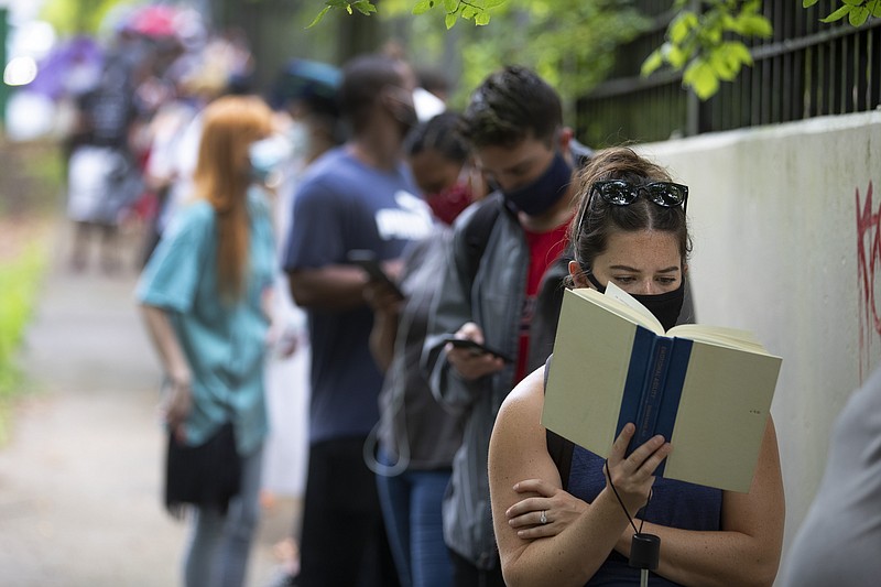 Kelsey Luker reads as she waits in line to vote, Tuesday, June 9, 2020, in Atlanta. Luker said she had been in line for almost two hours. (AP Photo/John Bazemore)