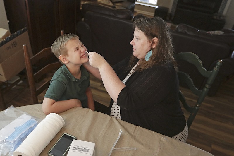 Mendy McNulty swabs the nose of her son, Andrew, 7, Tuesday, July 28, 2020, in their home in Mount Juliet, Tenn. Six thousand U.S. parents and kids are swabbing their noses twice a week to answer some of the most vexing mysteries about the coronavirus. The answers could help determine the safety of in-class education during the pandemic. (AP Photo/Mark Humphrey)