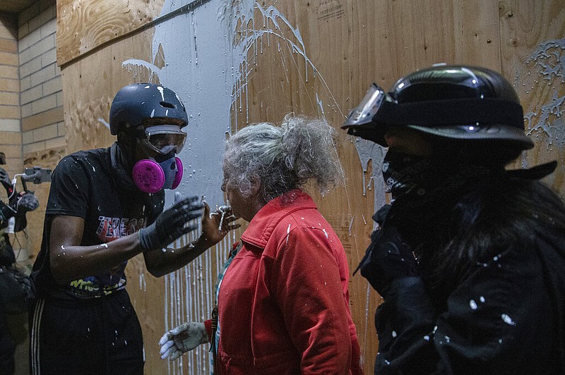 A woman who lives in a Portland neighborhood targeted by protesters argues with a few black-clad demonstrators after being splashed with white paint in front of a Portland Police Bureau precinct that was being vandalized, late Thursday, Aug. 6, 2020. The woman was trying to stop the protesters from vandalizing the building when she was hit with the paint.(Mark Graves /The Oregonian via AP)