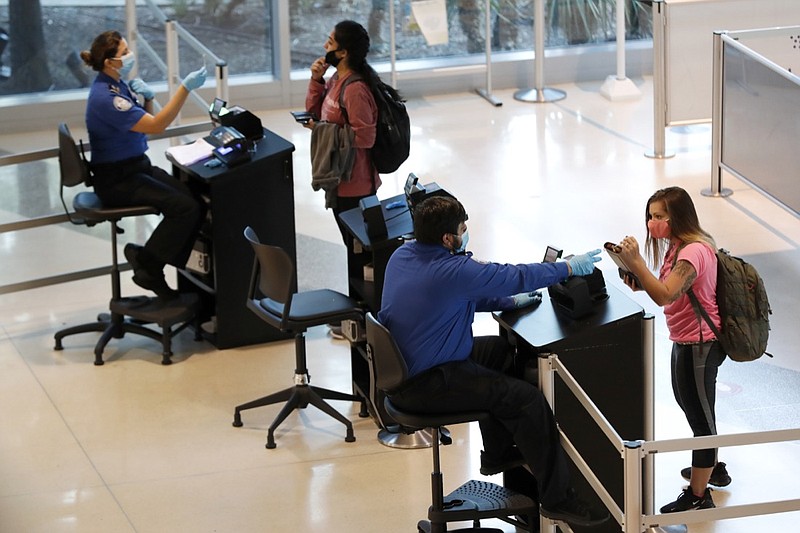 TSA agents help travelers as they clear security for flights out of Love Field in Dallas, Wednesday, June 24, 2020. (AP Photo/Tony Gutierrez)