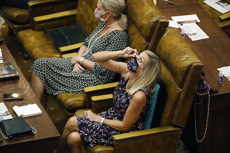 Rep. Dana McLean, R-Columbus, takes advantage of a brief recess at the Legislature to use some eyedrops while staying face masked and maintaining some social distance from row mate Rep. Jill Ford, R-Madison, Monday, Aug. 10, 2020, at the Capitol in Jackson, Miss. The legislators were in Jackson to finish the final parts of a state spending plan for the budget year that began July 1, and to override a number of passed legislation vetoes by Gov. Tate Reeves. (AP Photo/Rogelio V. Solis)