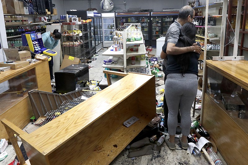 The Associated Press / Yogi Dalal hugs his daughter Jigisha as his other daughter, Kajal, left, bows her head at the family's food and liquor store Monday, after the usiness was vandalized following a night of looting and unrest.