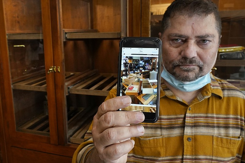 Neil Mehra, owner of the Hubbard & State Cigar Shop, near Chicago' Magnificent Mile, stands nears an empty humidor on Wednesday, Aug. 12, 2019, holding a cell phone image of his shop after looters stole thousands of dollars worth of merchandise and cash. “When I got here and saw what they’d done, I almost cried,” said Mehra. “This is my life. I really don’t know if we’re going to survive this.” (AP Photo/Charles Rex Arbogast)