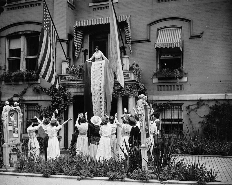 In this Aug. 19, 1920 photo made available by the Library of Congress, Alice Paul, chair of the National Woman's Party, unfurls a banner after the ratification of the 19th Ammendment, from a balcony at the NWP's headquarters in Washington. (The Crowley Company/Library of Congress via AP)