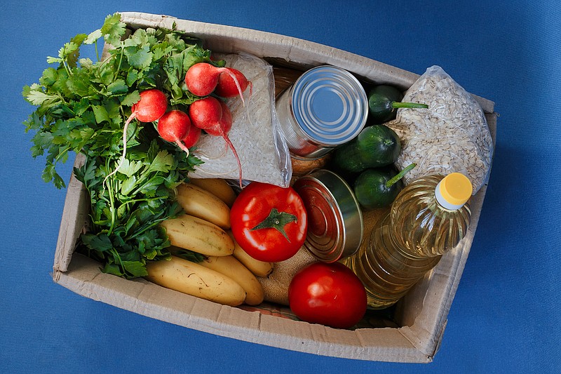 Donation box with food on a blue background. Fruits, vegetables, canned food, pasta and sunflower oil in a box. Social assistance with food. food tile food bank food assistance / Getty Images
