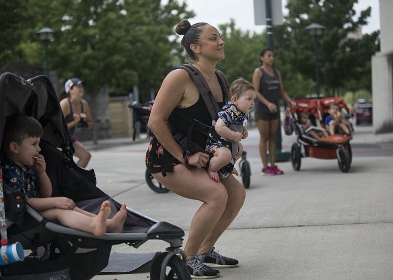 Staff photo by Troy Stolt / Analisa Shepard does squats while holding her 6-month-old son Elijah, as her son Asher, 2, sits in a stroller during Fit4Mom's Stroller Stride class in Coolidge Park on Friday, Aug. 14, 2020 in Chattanooga, Tenn. Stroller Strides is an exercise class for mothers of young children that allows mothers to get a workout in as their children are entertained.
