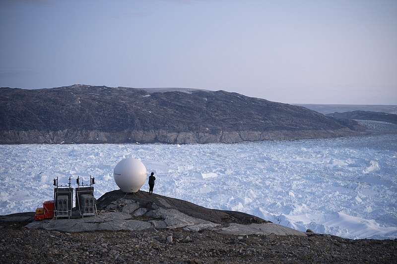 In this Aug. 16, 2019 file photo, a woman stands next to an antenna at an NYU base camp at the Helheim glacier in Greenland. According to a study released on Thursday, Aug. 20, 2020, Greenland lost a record amount of ice during an extra warm 2019, with the melt massive enough to cover California in more than four feet (1.25 meters) of water. (AP Photo/Felipe Dana)