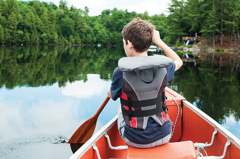 Getty Images / A young boy paddles in a calm lake.