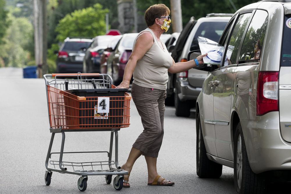 Staff photo by C.B. Schmelter / Mary Vickery passes out bags containing strainers, vegetable brushes and recipes as people wait in line to receive food from the Red Bank Community Food Pantry at Red Bank United Methodist Church on Thursday, Aug. 20, 2020 in Chattanooga, Tenn.