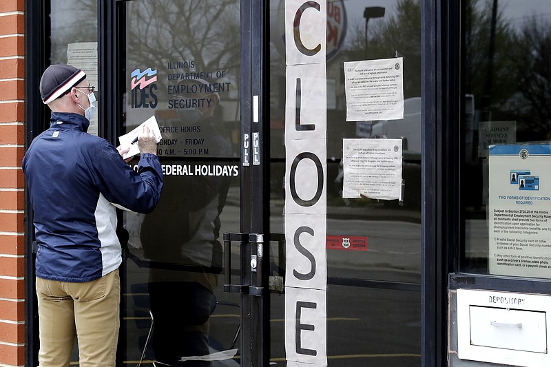 FILE - In this April 30, 2020 file photo, a man writes information in front of Illinois Department of Employment Security in Chicago. It's the paradox of a pandemic that has crushed the U.S. economy: There are 12.9 million job losses and a dangerous rash of closed business, yet the personal finances of many Americans have remained strong, and in some ways have even improved. A new poll by The Associated Press-NORC Center for Public Affairs Research shows that 45% of Americans say they're setting aside more money than usual. Twenty-six percent are paying down debt faster than they were before the coronavirus pandemic. In total, about half of Americans say they've either saved more or paid down debt. (AP Photo/Nam Y. Huh, File)