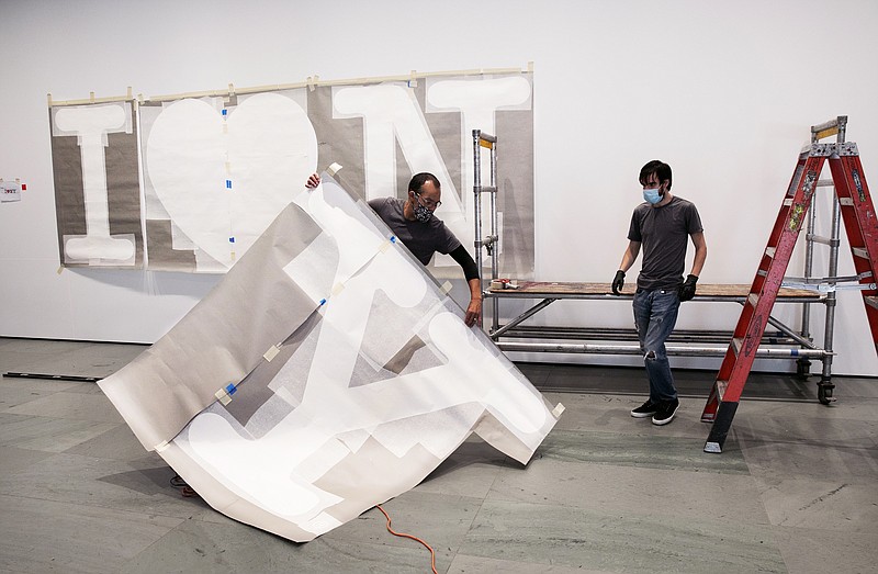 George Vealsquez, left, and Charles Lester install templates for "I Love NY" at the entrance to the Museum of Modern Art, Thursday, Aug. 20, 2020, in New York. The work by graphic designer Milton Glaser will be done in red for the heart and black for the lettering. MOMA reopens Aug. 27, 2020. (AP Photo/Mark Lennihan)